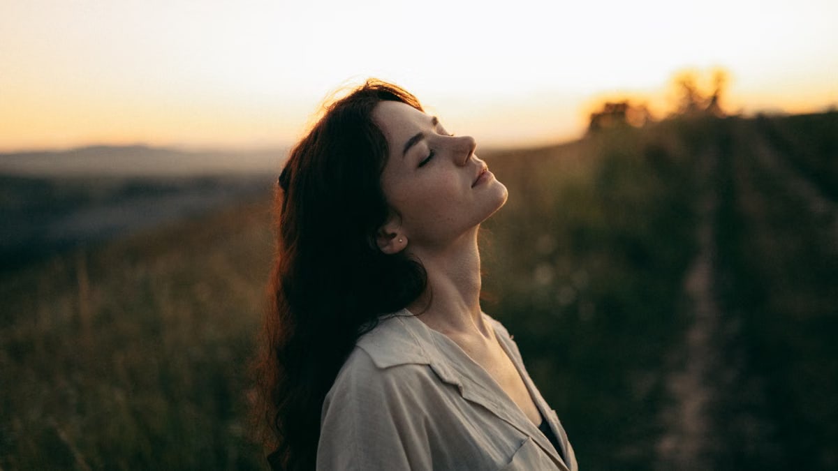 A serene woman with head tilted back, savoring the warm sunset in a field.